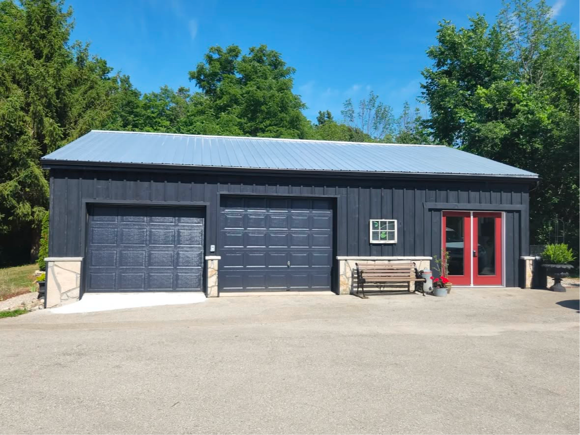 Dark blue garage with metal roof and red double doors. Bench and potted plants in front.