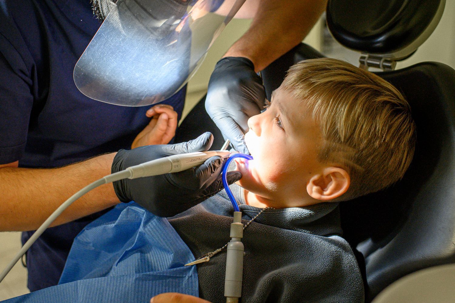 Dentist examining a child’s mouth with a bright light and dental tools in a clinic