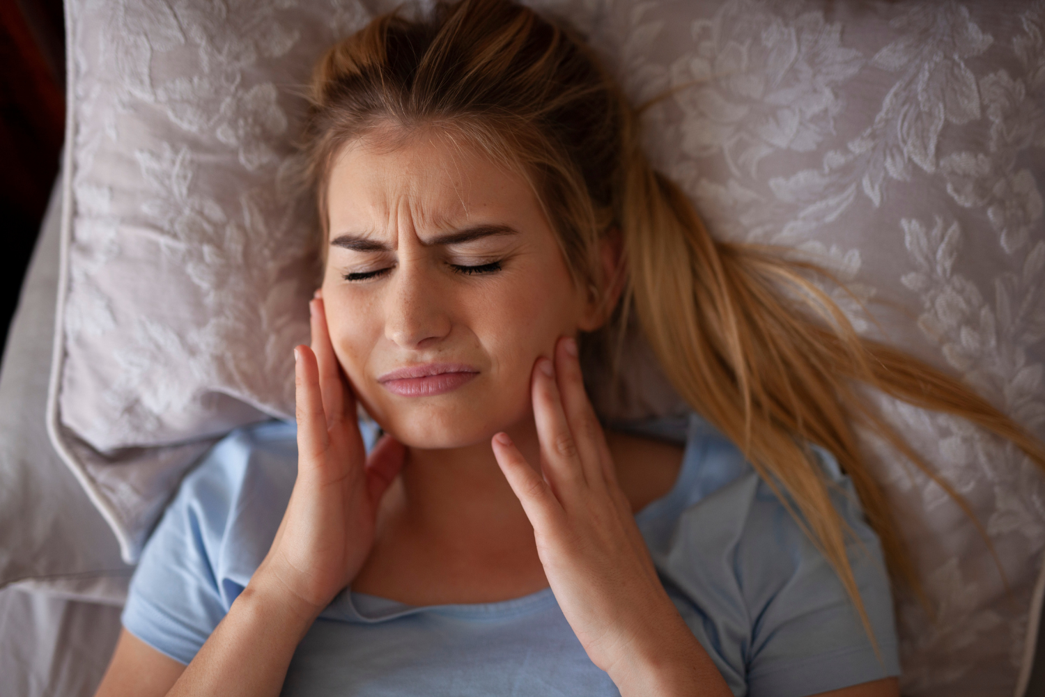 Woman grimacing and holding her cheek, suggesting tooth pain, indoors.