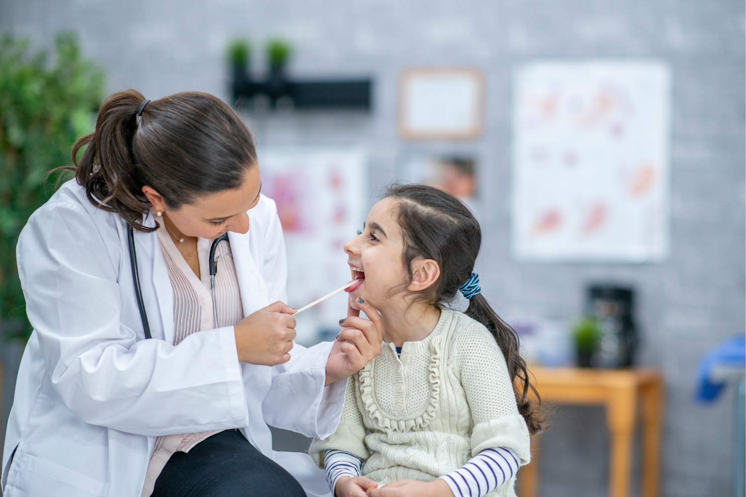 Doctor examining a smiling child’s throat in a clinic