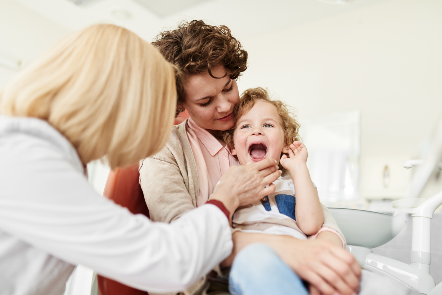 Adult and child smiling in a bright clinic, with a blonde clinician leaning in beside them