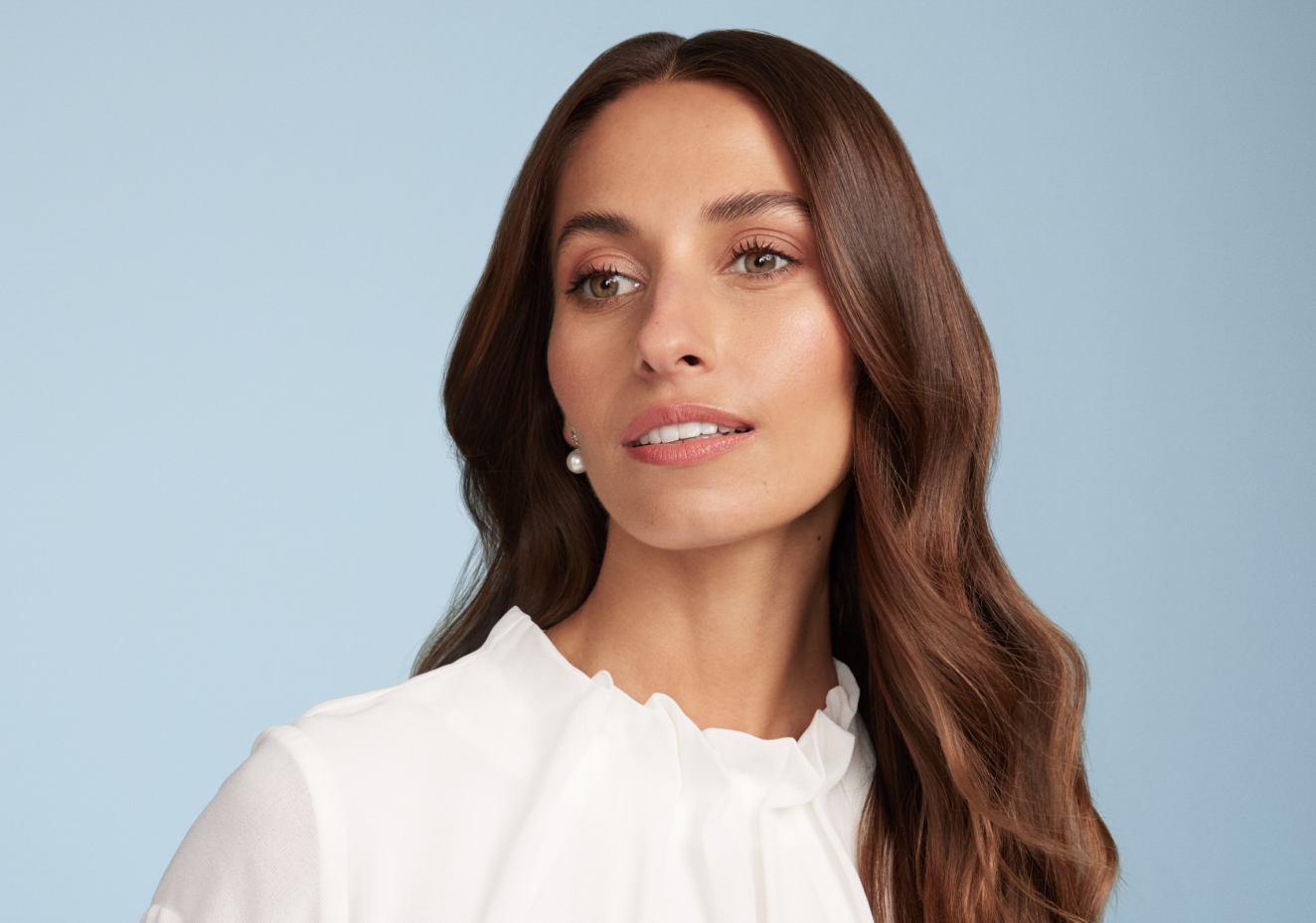 Woman with long brown hair wearing a white top against a light blue background