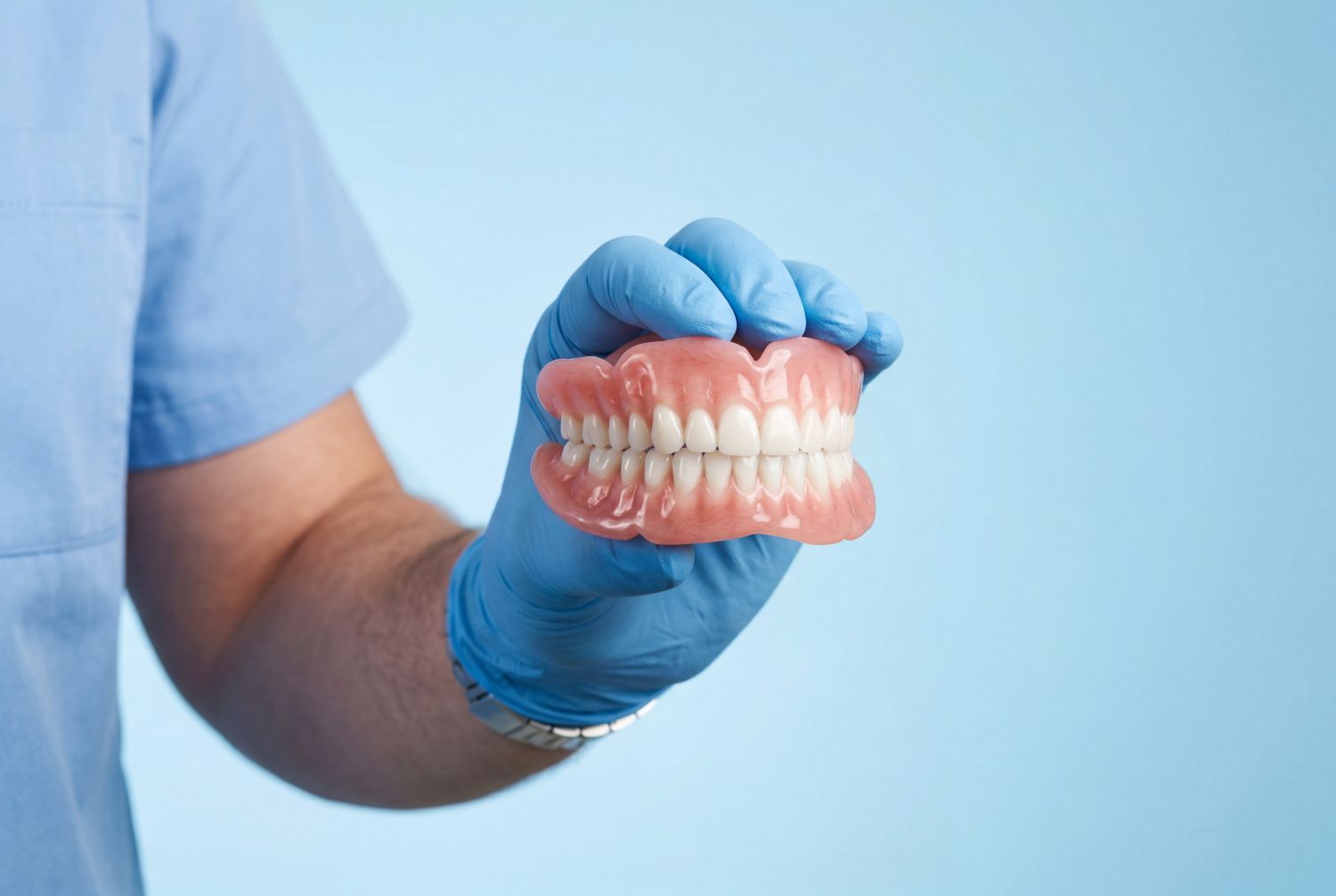 Gloved hand holding dental dentures against a light blue background