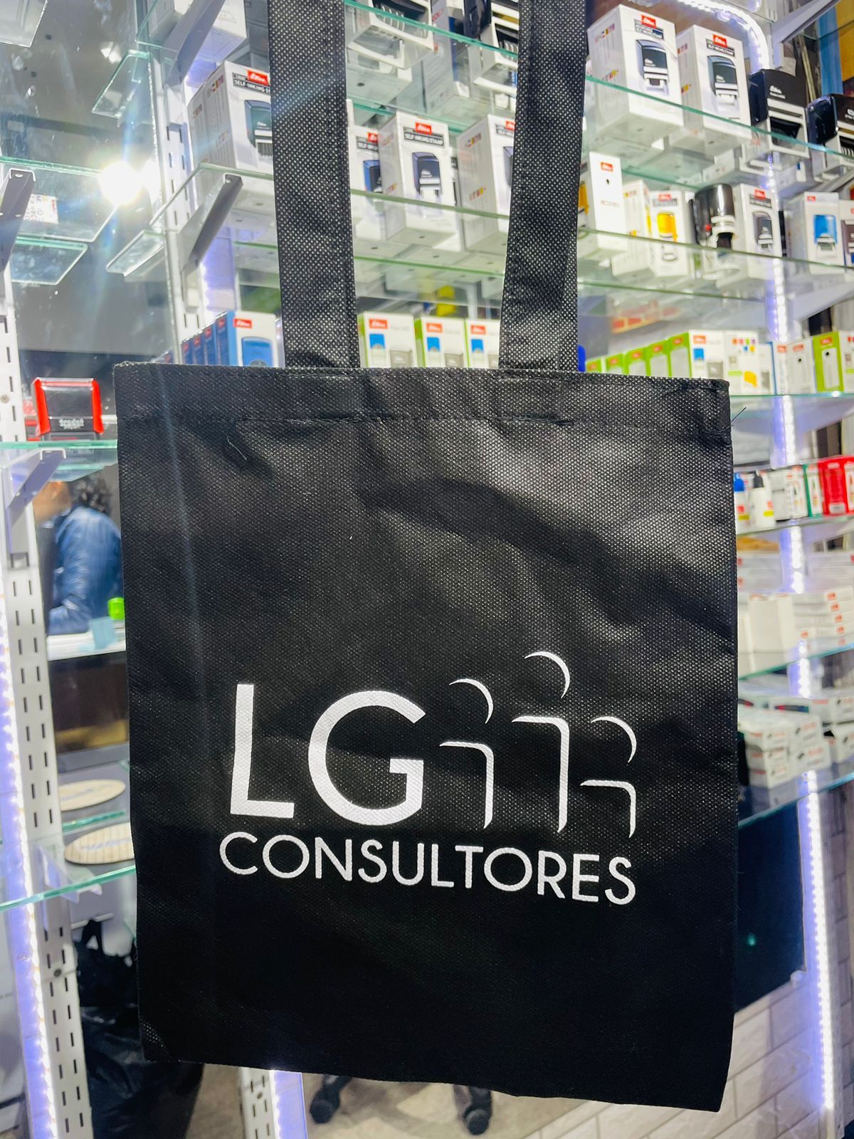 Bolsa de mano negra con logo “LG Consultores” frente a un exhibidor de tienda.