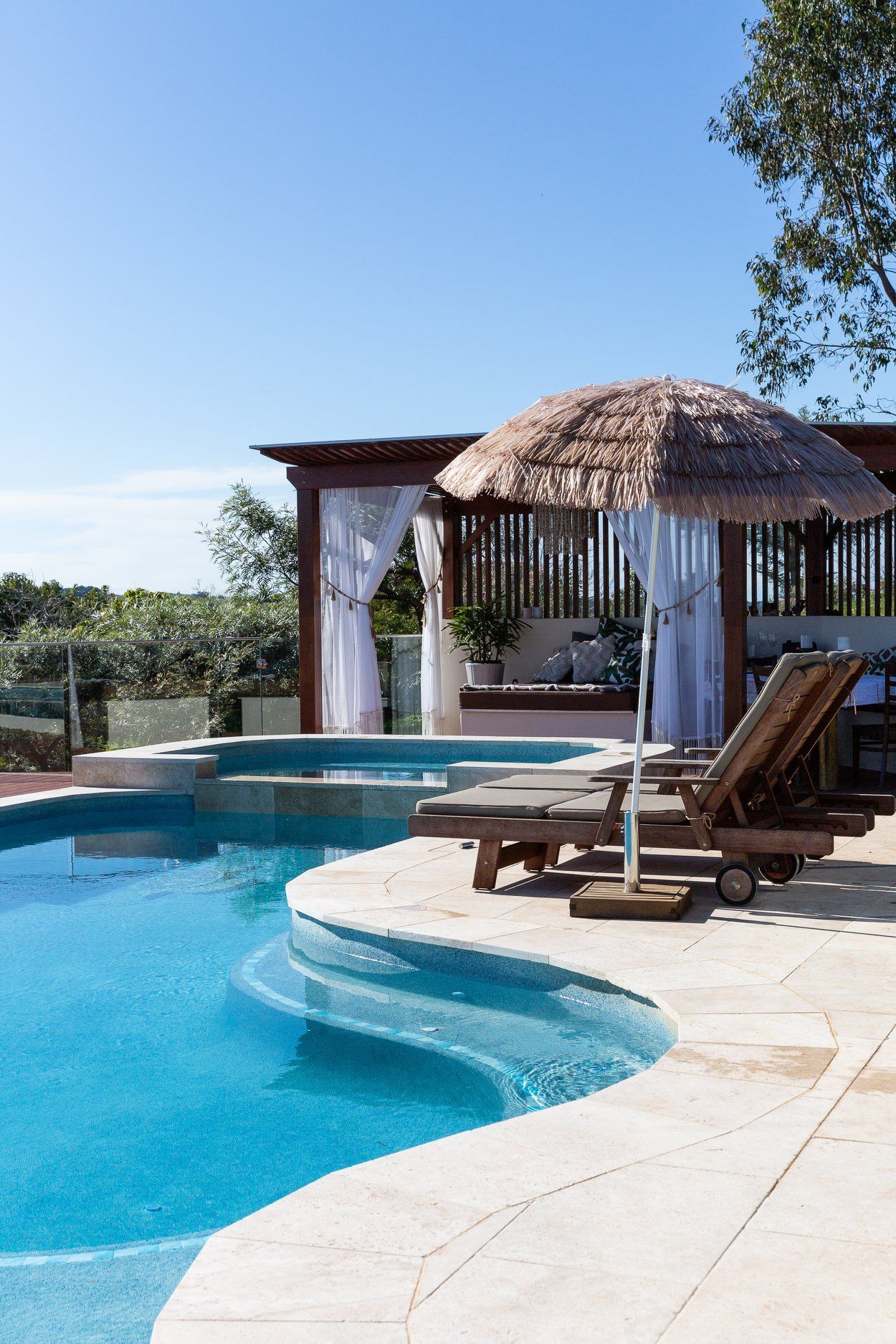 A Large Swimming pool with chairs and Umbrellas Around it — Profile Pools & Landscaping In Byron Bay, NSW