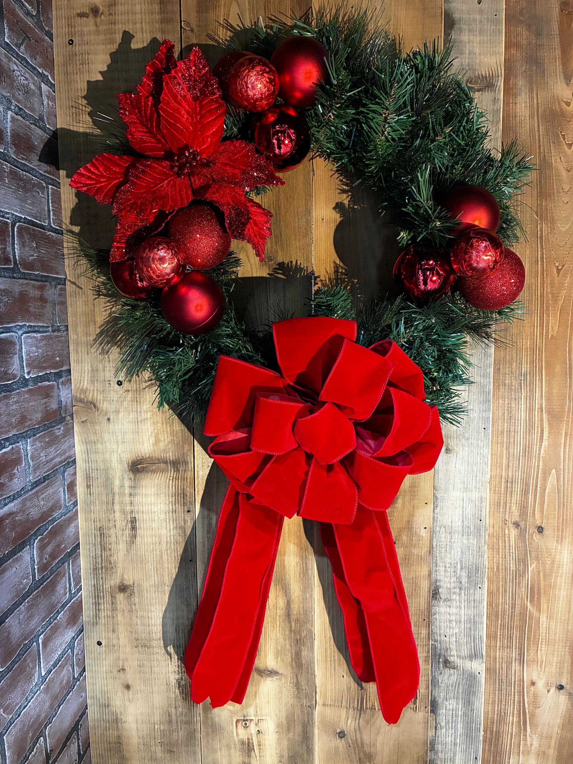 Red holiday wreath with gold, red ornaments and a large red bow on a wooden background