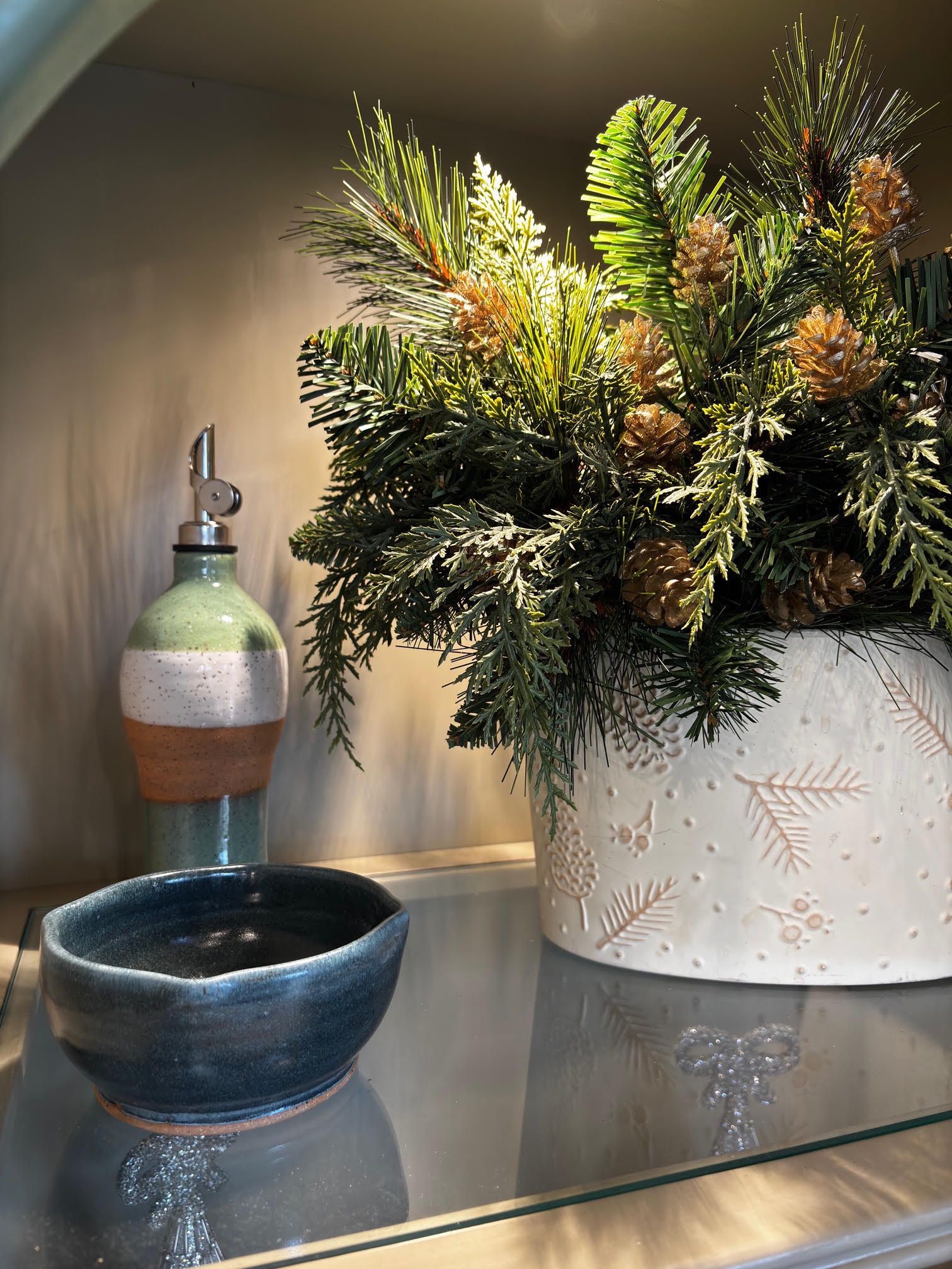 Decorative floral arrangement in a white vase beside a blue bowl and glass bottle on a shelf