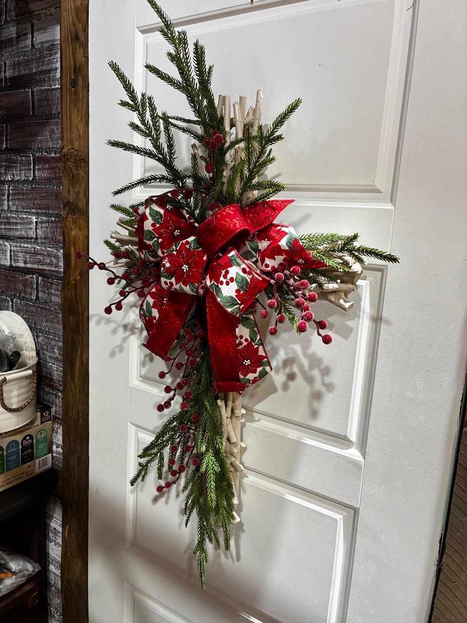 Red holiday swag with ribbon and berries hanging on a white paneled door