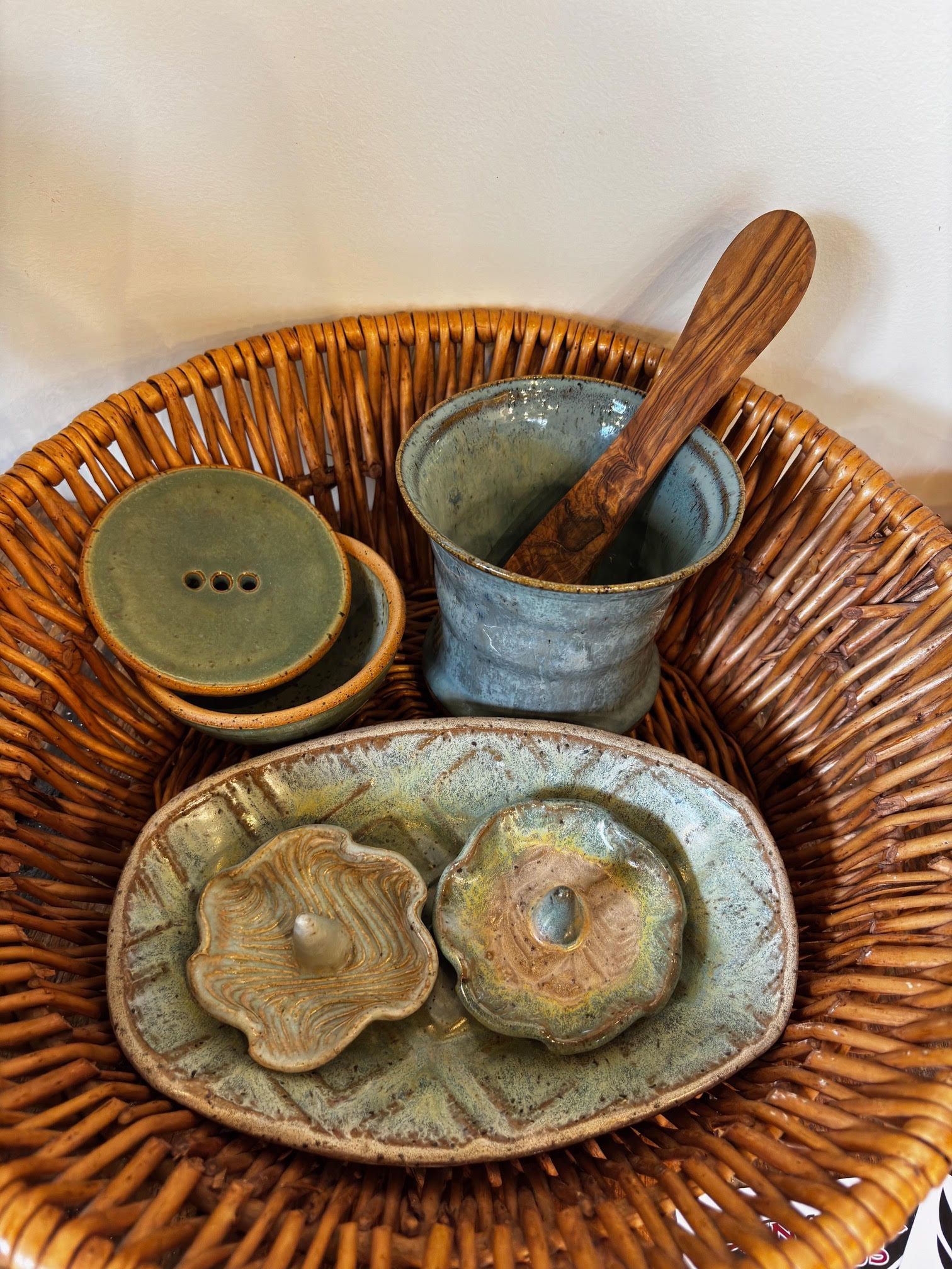 Wicker basket with handmade ceramic dishes and bowls in muted green and brown tones