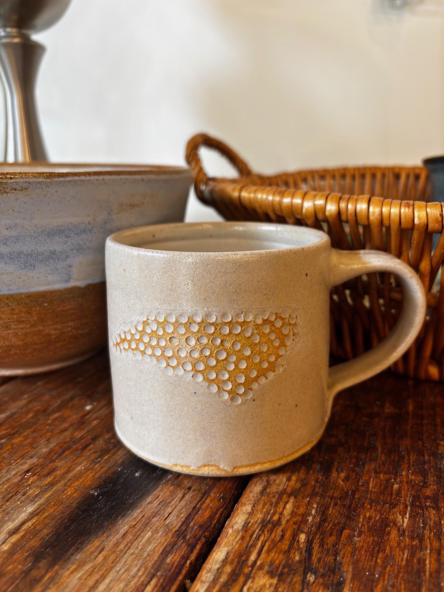 Beige ceramic mug with honeycomb pattern on a wooden table beside a wicker basket and pottery bowl