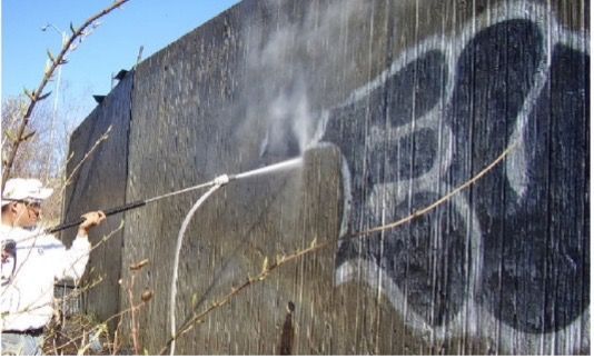 Man power washing graffiti off a concrete wall.