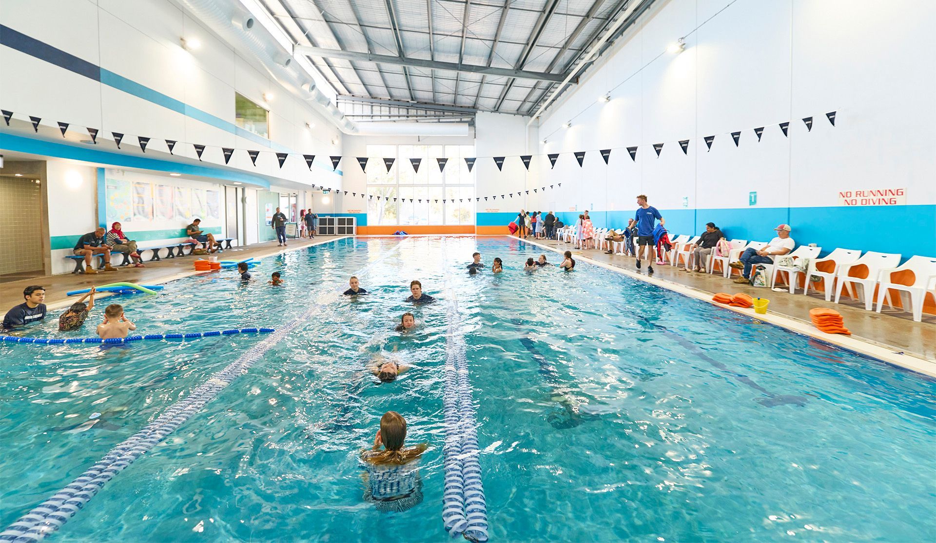 A large indoor swimming pool with light and bright floor to ceiling windows at the far end