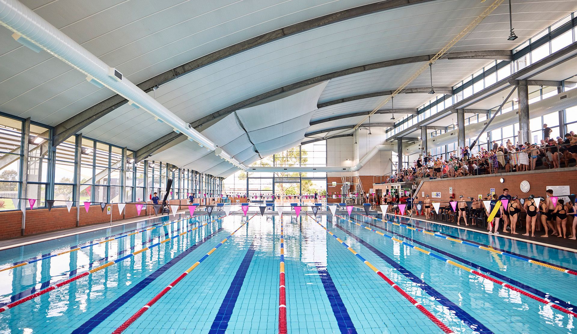 Large 50m swimming pool with high curved ceilings and stadium seating along the right hand side