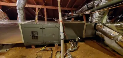 HVAC furnace and ductwork in an unfinished attic with exposed insulation and rafters