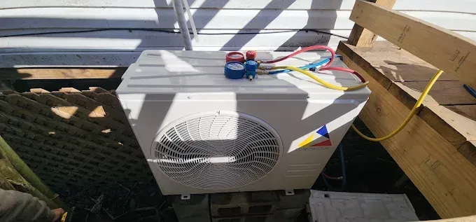 White HVAC unit with a fan on a rooftop, connected to colorful wires and a wooden pallet nearby