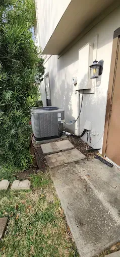 Narrow side yard beside a house with an outdoor AC unit, concrete path, and small grassy strip