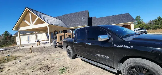 Black truck parked by a house under construction with exposed framing and dirt lot