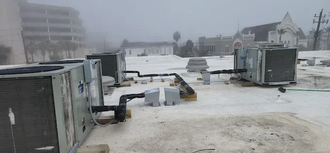 Snow-covered industrial yard with shipping containers, equipment, and buildings in foggy weather