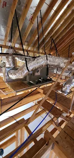 Exposed ceiling ducts and insulation in an unfinished attic with wooden rafters and hanging straps