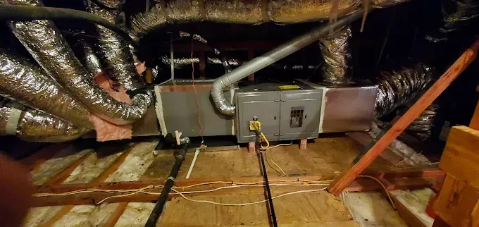 Attic HVAC unit with insulated ducts, wiring, and a corrugated metal vent panel