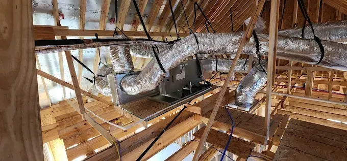 Attic with exposed wooden beams, insulation ducts, and HVAC equipment under construction