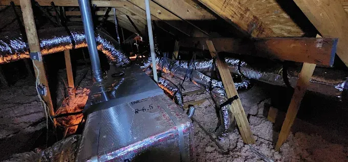 Damaged attic with exposed rafters, a hanging duct, and fire-damaged debris on the floor.