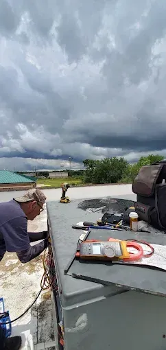 Person on a boat holding a pole, with stormy clouds over turquoise water and a distant shoreline.