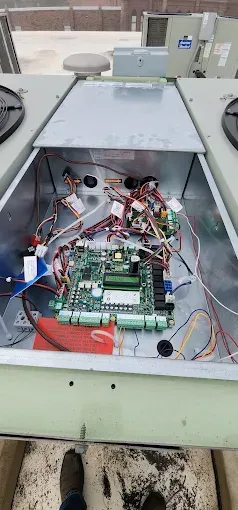 Open metal electrical cabinet with exposed circuit boards, wires, and components on a rooftop.