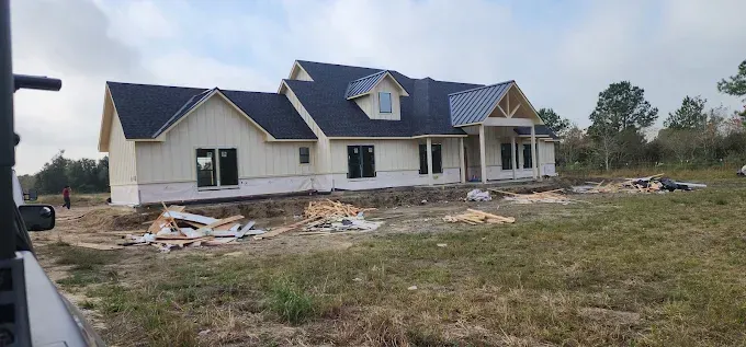 Partially built house with blue roof, damaged exterior, and construction debris in a grassy lot