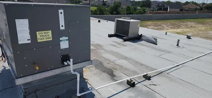 Rooftop HVAC unit and white membrane roof with vents and piping under bright daylight