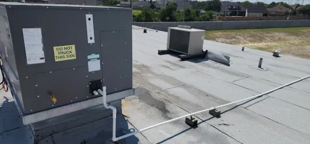 Rooftop HVAC unit and ductwork on a flat white roof under daylight.