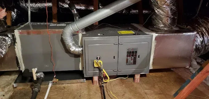HVAC furnace in attic with exposed ductwork and yellow service hose connected