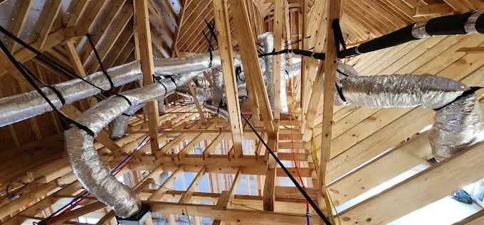 Exposed wooden rafters and silver HVAC ducts inside an unfinished attic ceiling