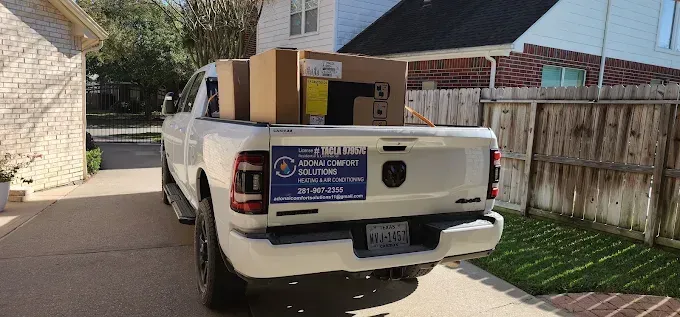 White pickup truck parked in a driveway with boxes stacked in the bed near a wooden fence.