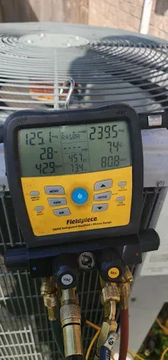 Yellow-and-black HVAC manifold gauge on an outdoor AC unit, with hoses connected and display readings visible
