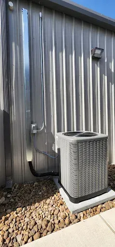Outdoor air conditioning unit beside a metal building wall and electrical conduit
