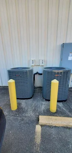 Two outdoor HVAC units behind yellow bollards against a beige wall.
