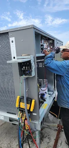 Technician inspecting open electrical equipment with bundled wires outdoors beside a gray utility unit
