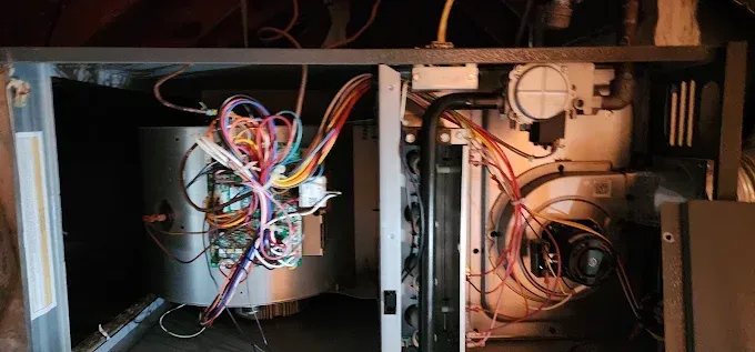 Open electrical panel with tangled multicolored wires and components inside a metal cabinet