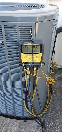 Yellow HVAC gauges connected to an outdoor air conditioning unit with black hoses