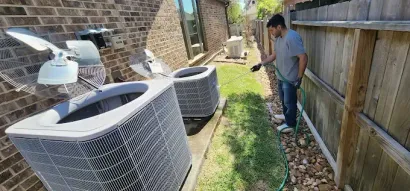 Man working beside outdoor air conditioning units along a fenced side yard