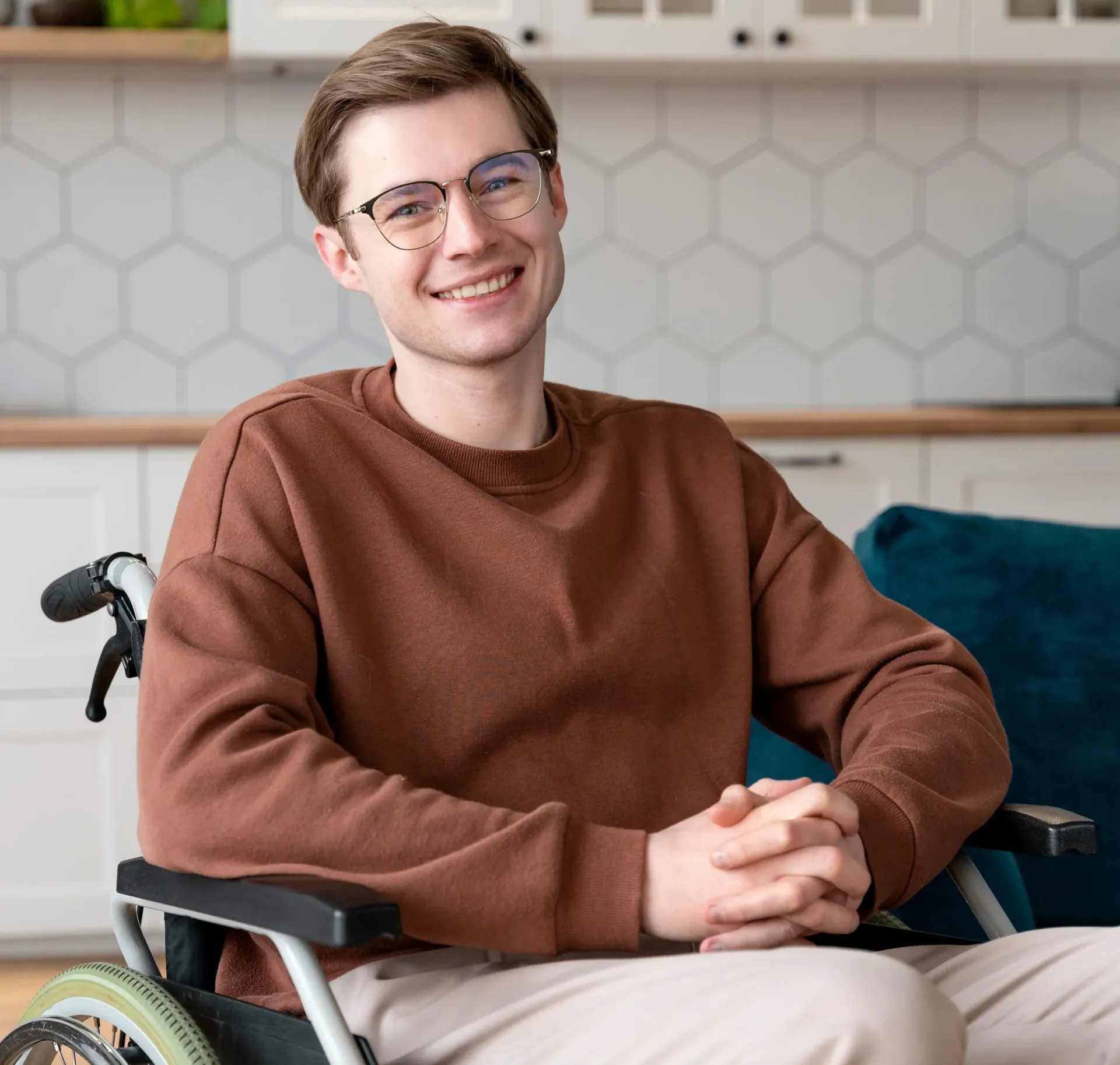 A young man is sitting in a wheelchair wearing glasses and smiling.