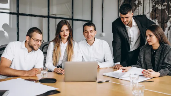 A group of people are sitting around a table looking at a laptop.