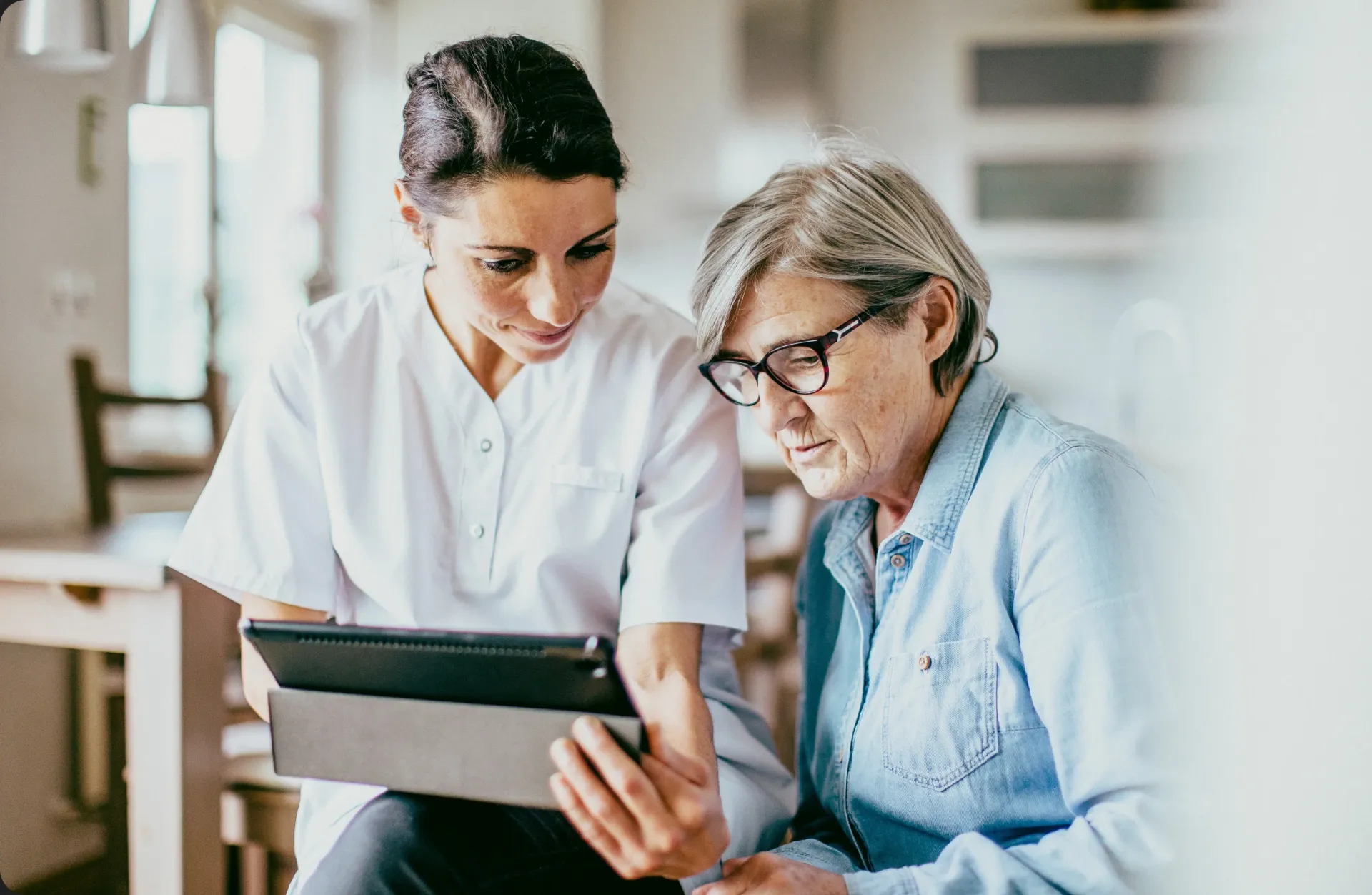 A nurse is teaching an elderly woman how to use a tablet computer.
