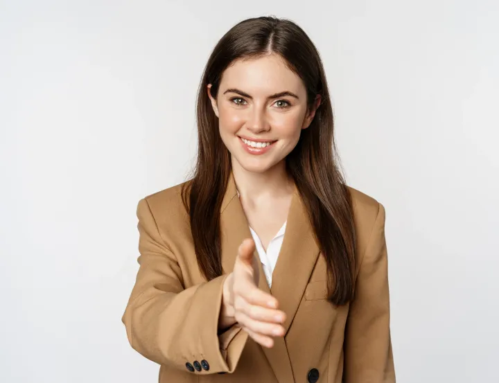 A woman in a suit is reaching out her hand to shake someone 's hand.