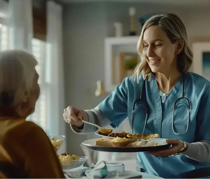 A nurse is serving food to an elderly woman at a table.