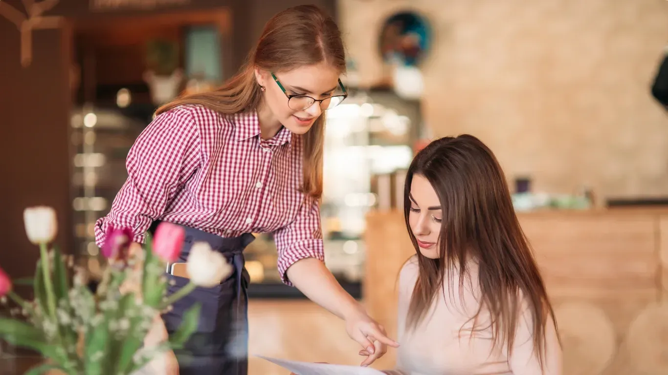 Two women are sitting at a table in a restaurant looking at a piece of paper.