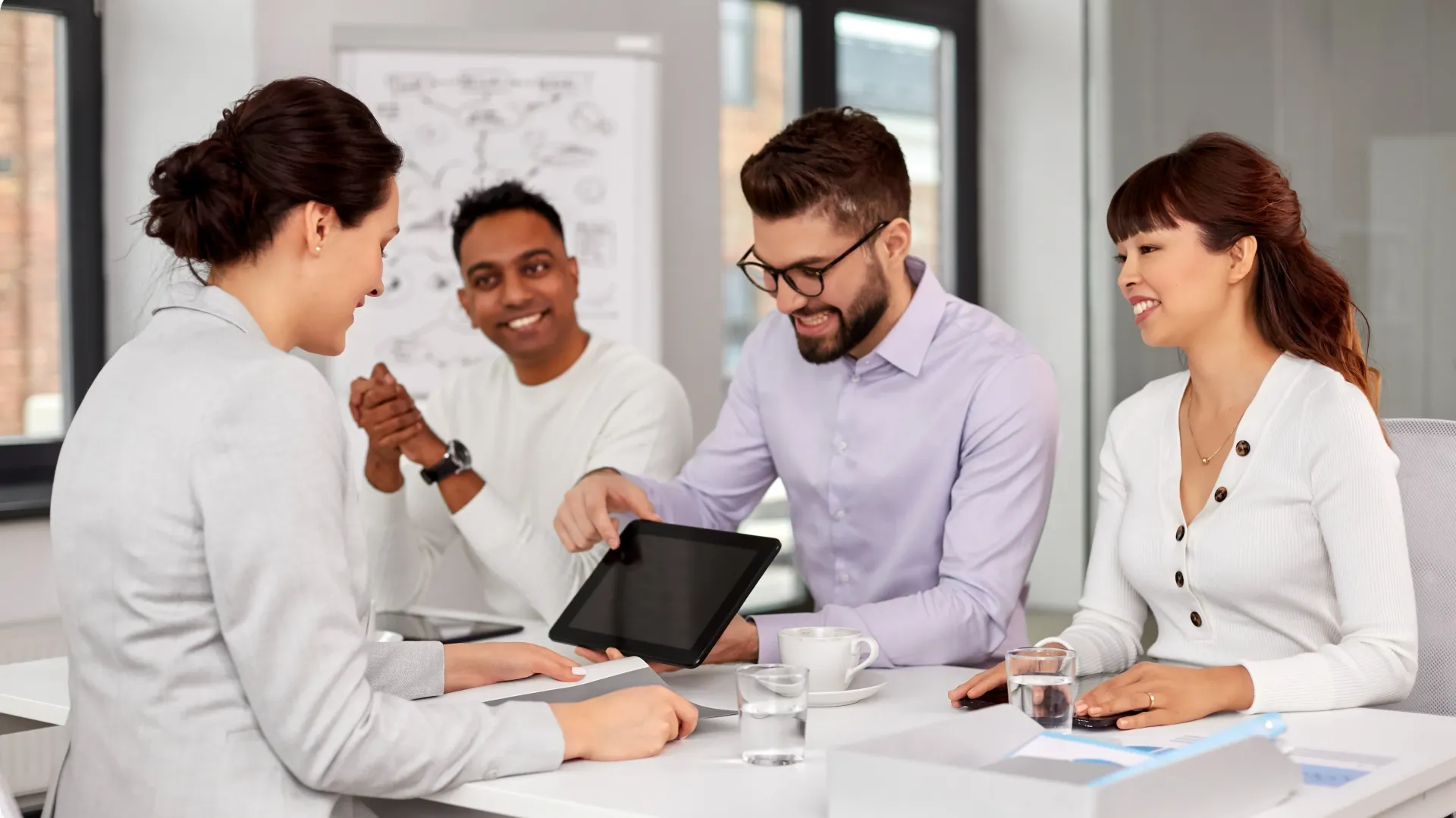 A group of people are sitting around a table looking at a tablet.