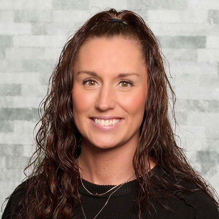 Smiling woman with wet brown hair wearing a black top against a light gray background