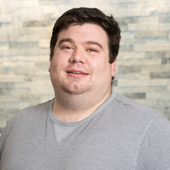 Portrait of a smiling person in a gray shirt against a softly blurred stone wall background